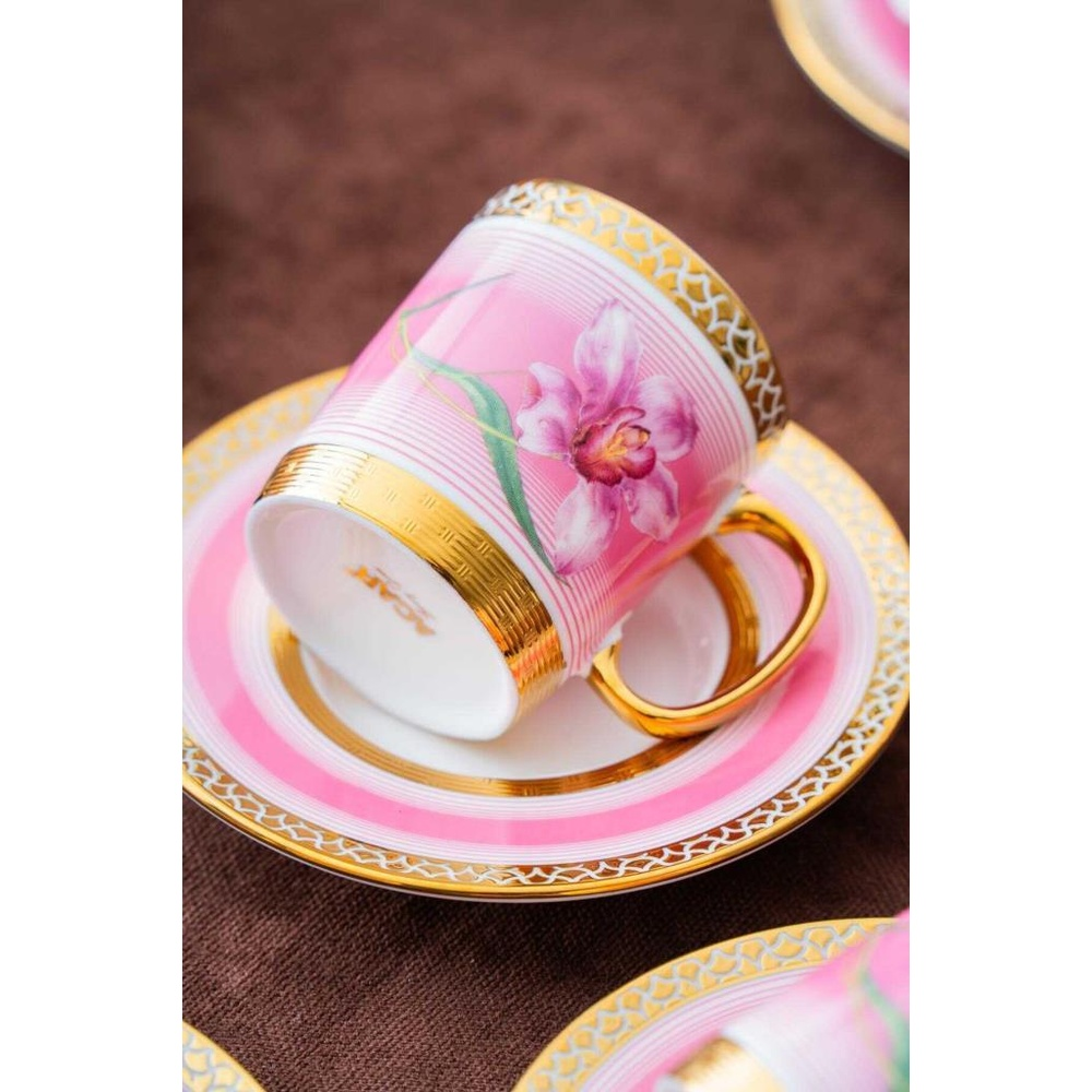 Orkide desenli, altın süslemeli açık pembe fincan, tabağın üzerinde duruyor.