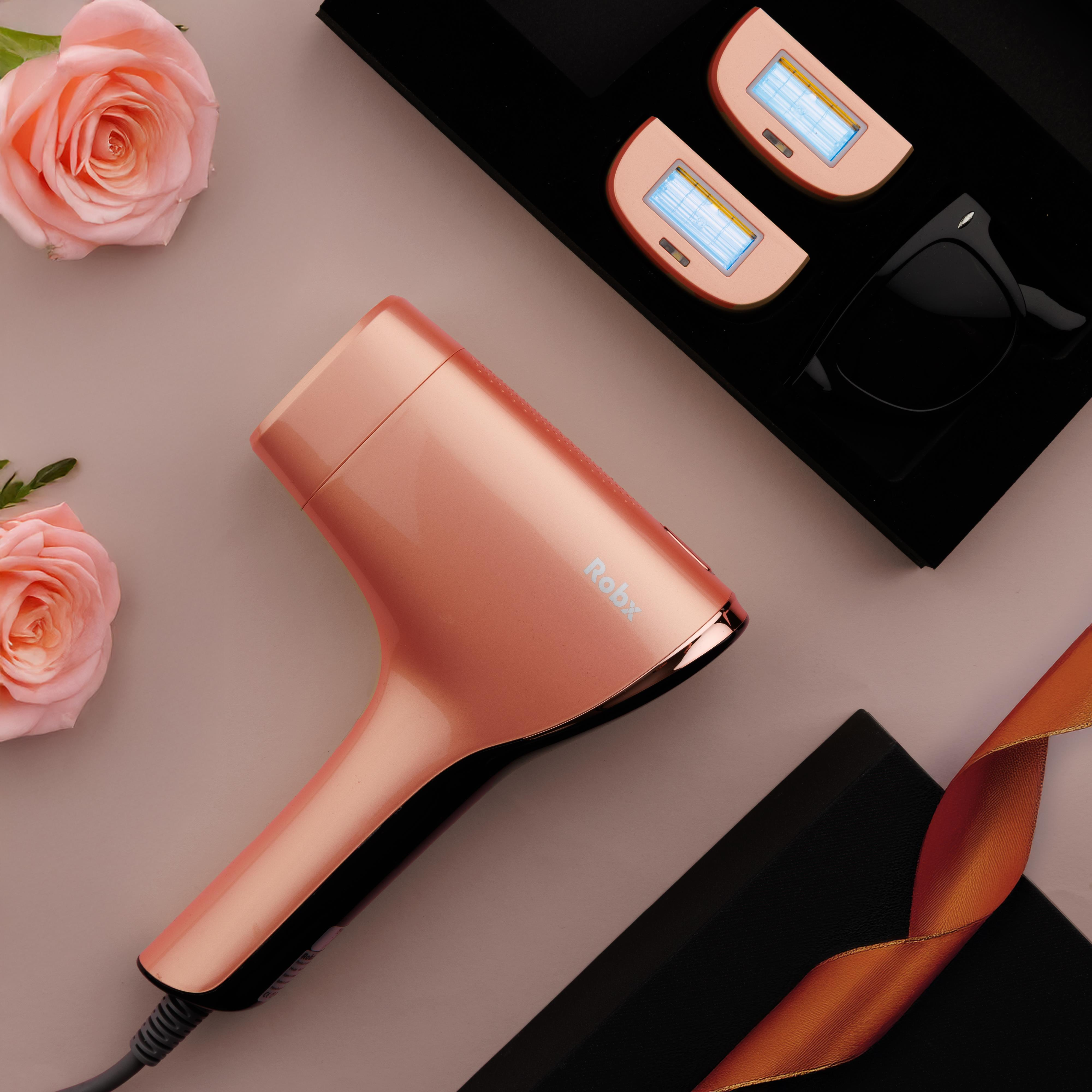 Rose gold saç kurutma makinesi, iki IPL cihazı, güneş gözlüğü, pembe güller ve kurdele pembe zeminde.