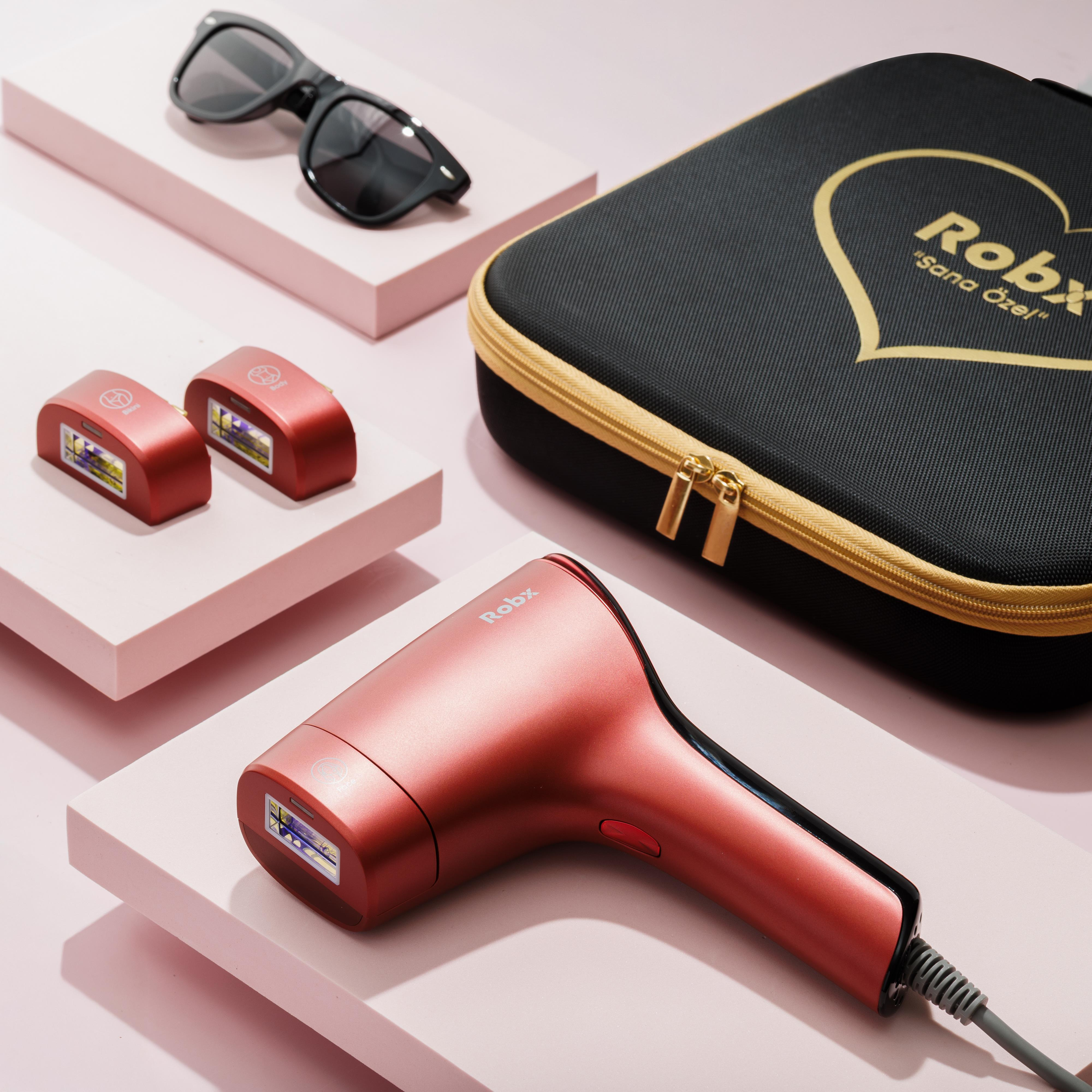 Rose gold epilasyon cihazı, iki kırmızı başlık, siyah güneş gözlüğü ve siyah çanta.