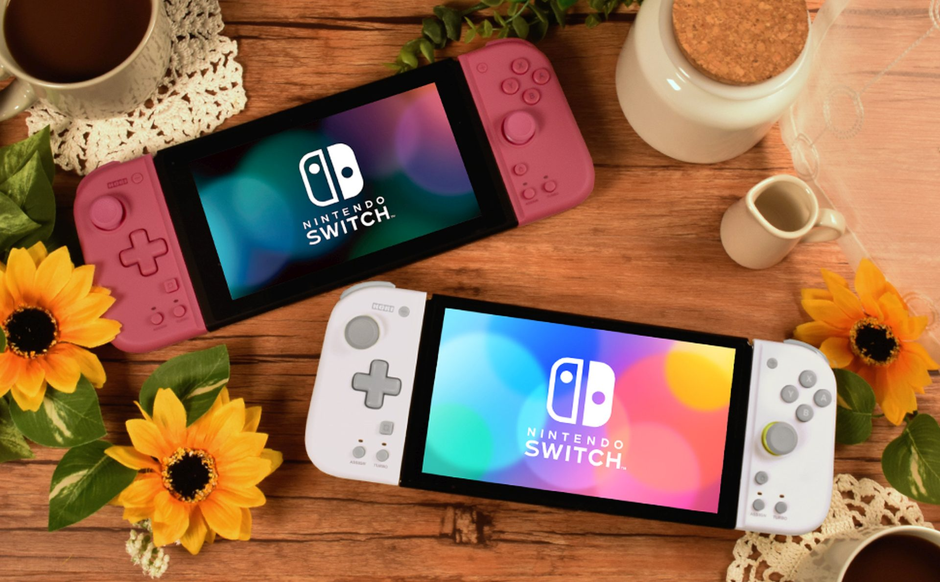 Dwie konsole Nintendo Switch, jedna różowa, jedna biała, z słonecznikami i kawą na drewnie.