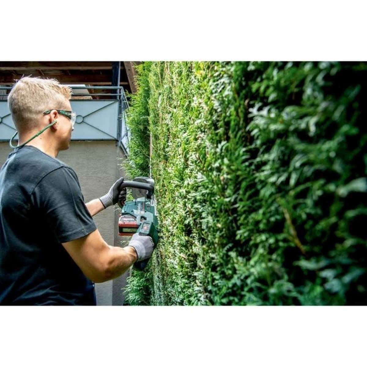 Mann trimmte Hecke mit elektrischem Hedge Trimmer, trug Schutzbrille und Handschuhe.