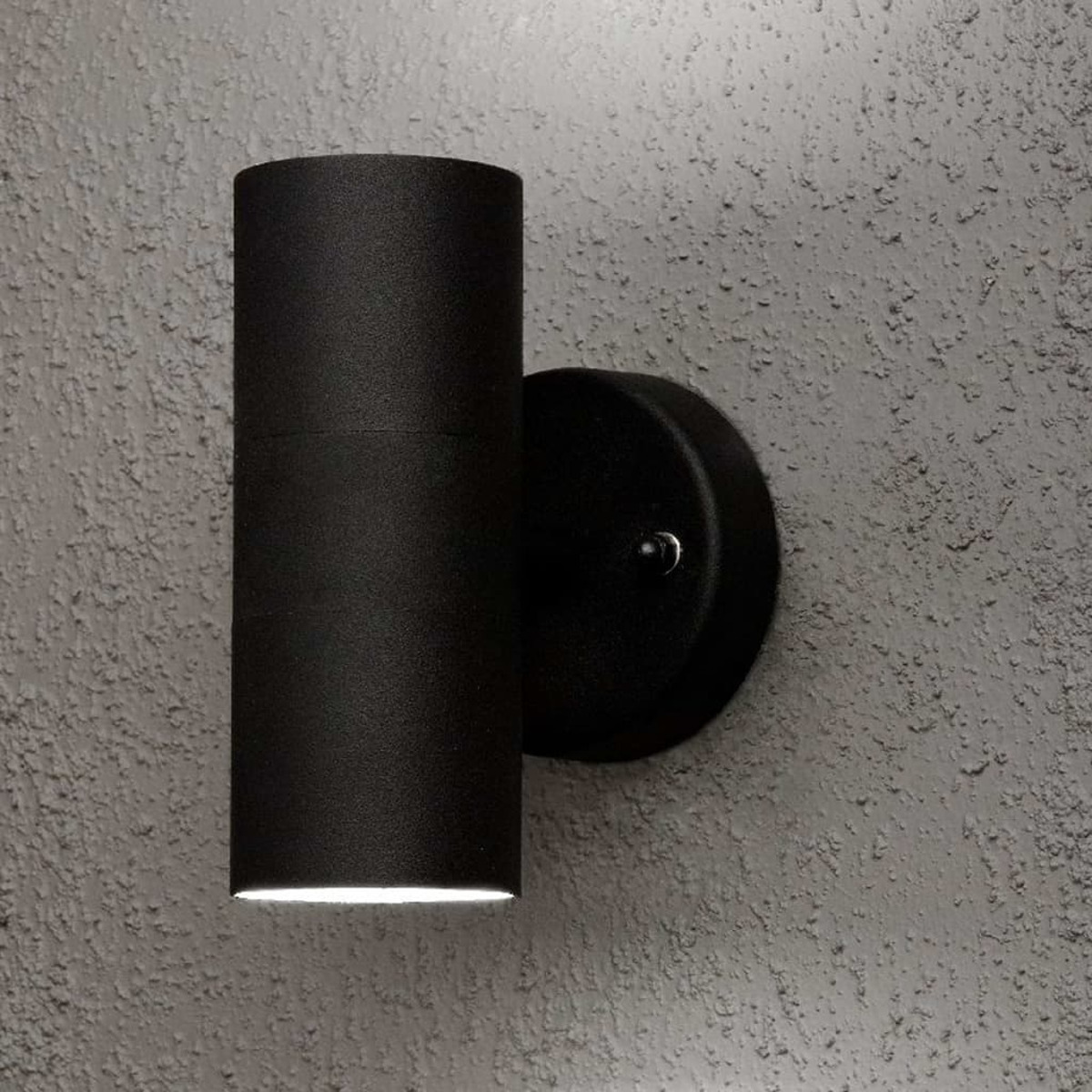 Eine schwarze zylindrische Wandleuchte mit strukturiertem grauen Hintergrund.