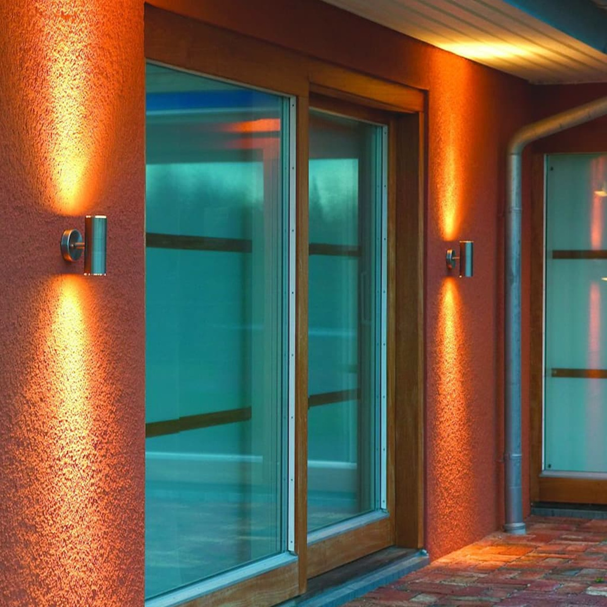 Zwei Wandleuchten beleuchten eine orangefarbene Wand neben einem Holzfenster.