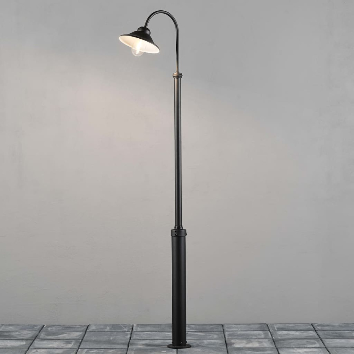 Eine schwarze Straßenlaterne mit gebogenem Arm und Glühbirne steht auf gepflastertem Boden.