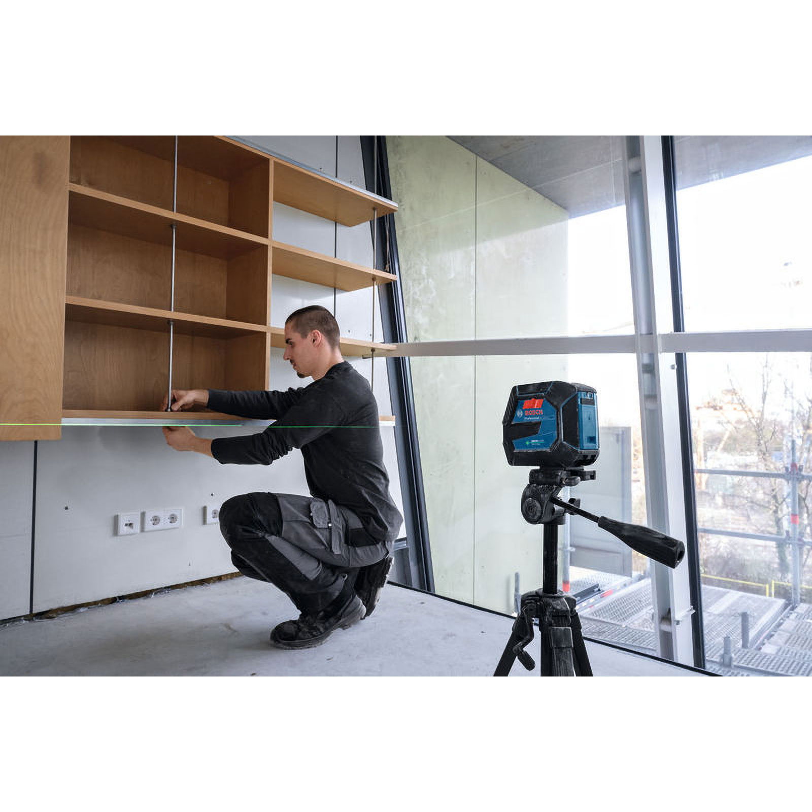 Mann montiert Regal mit Laser-Wasserwaage. Bosch-Laser auf Stativ.