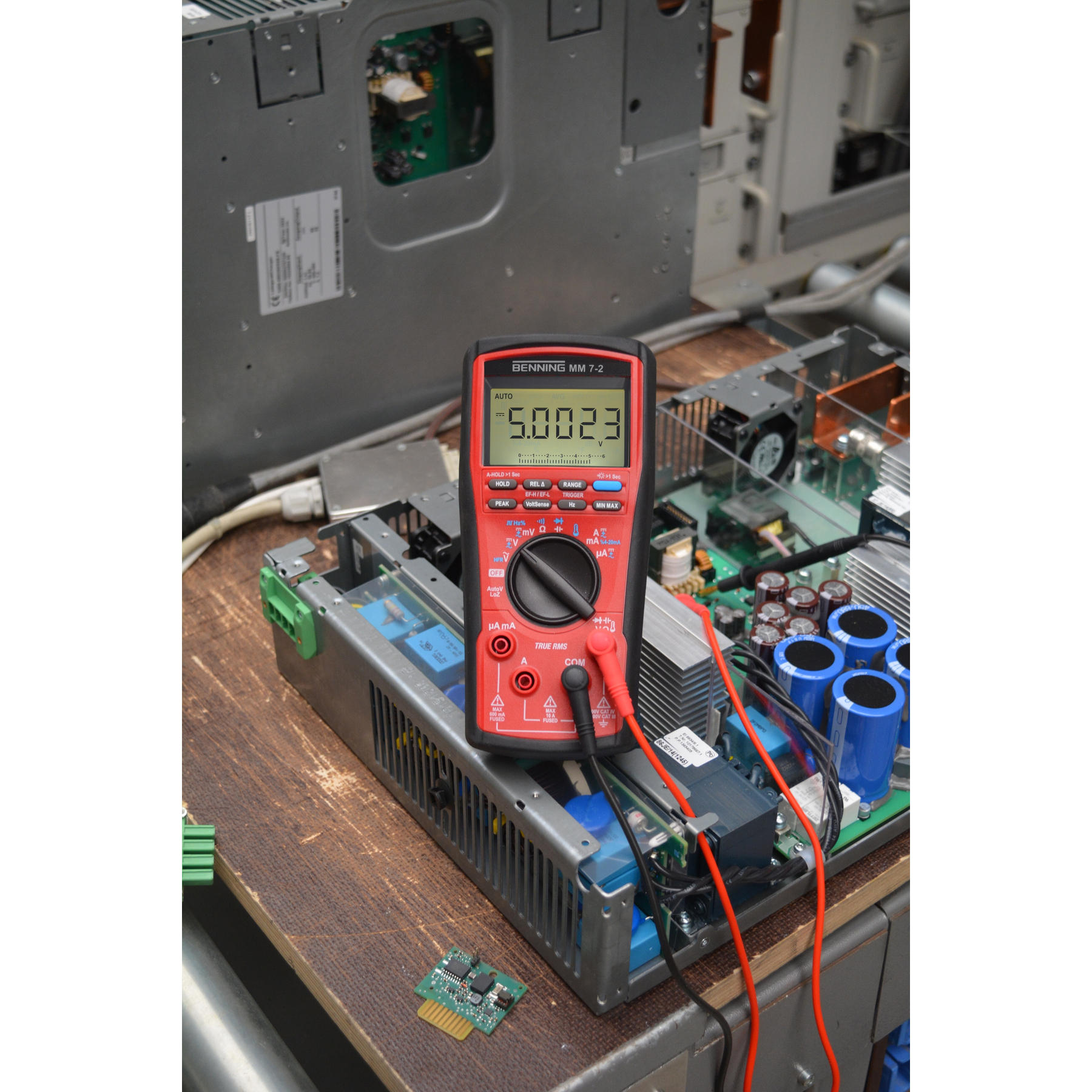 Ein rotes Multimeter mit der Anzeige 5.0023 V liegt auf elektronischen Bauteilen.