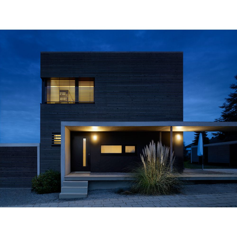 Modernes dunkles Haus mit Fenstern und Eingang im Abendlicht, Gras davor.