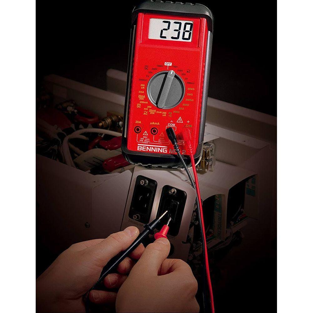 Ein rotes Multimeter mit der Anzeige 238 misst elektrische Werte in einem Kasten.