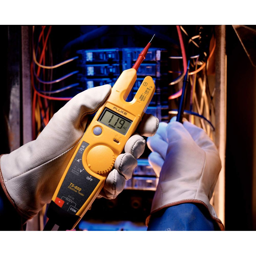 Ein Elektriker mit Handschuhen benutzt ein gelbes Fluke-Messgerät an Drähten.
