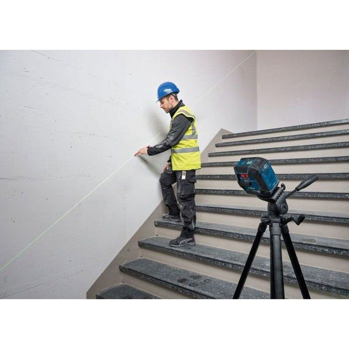 Ein Mann auf einer Treppe mit einem grünen Laserstrahl, der an der Wand verläuft.