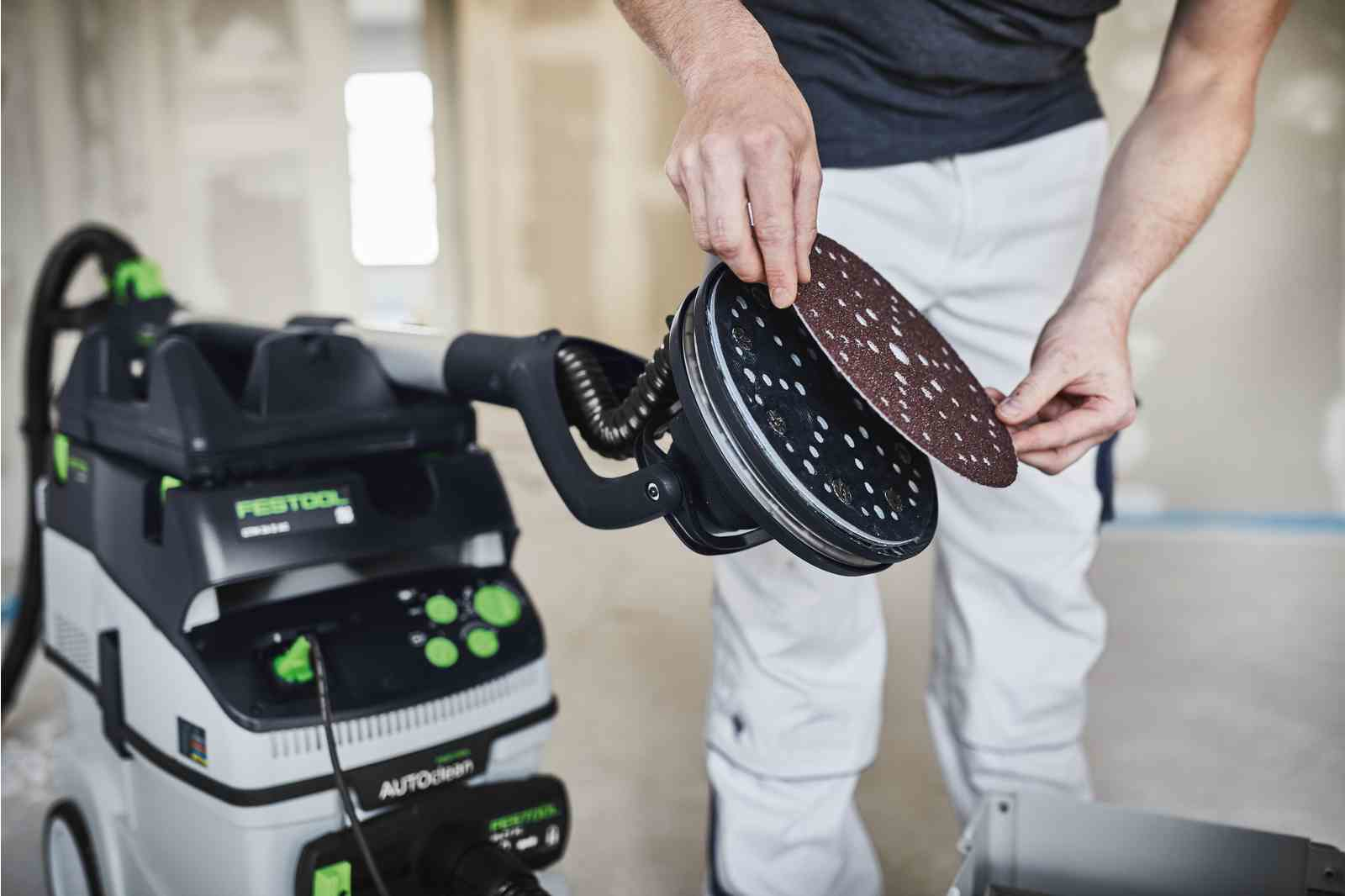 Mann wechselt Schleifpapier an einer Festool Maschine im Bauumfeld.