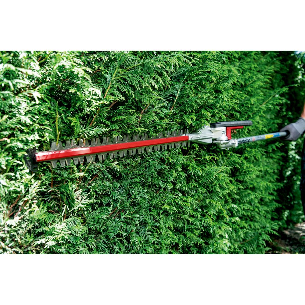 Ein Mann schneidet mit einer Heckenschere eine grüne Hecke.