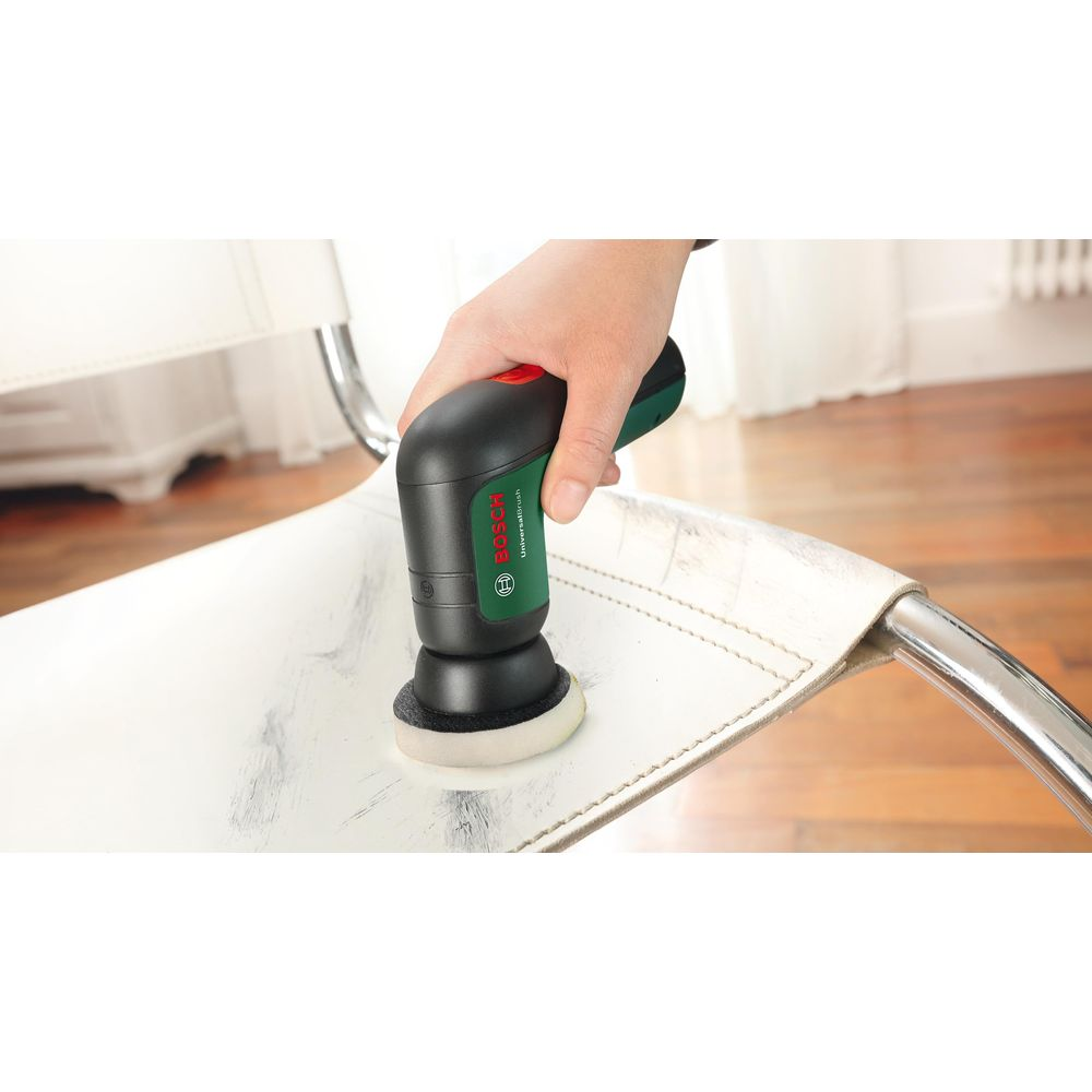 Eine Hand hält einen schwarzen Bosch Universal-Bürsten-Reiniger, der auf einem weißen Stuhl verwendet wird.