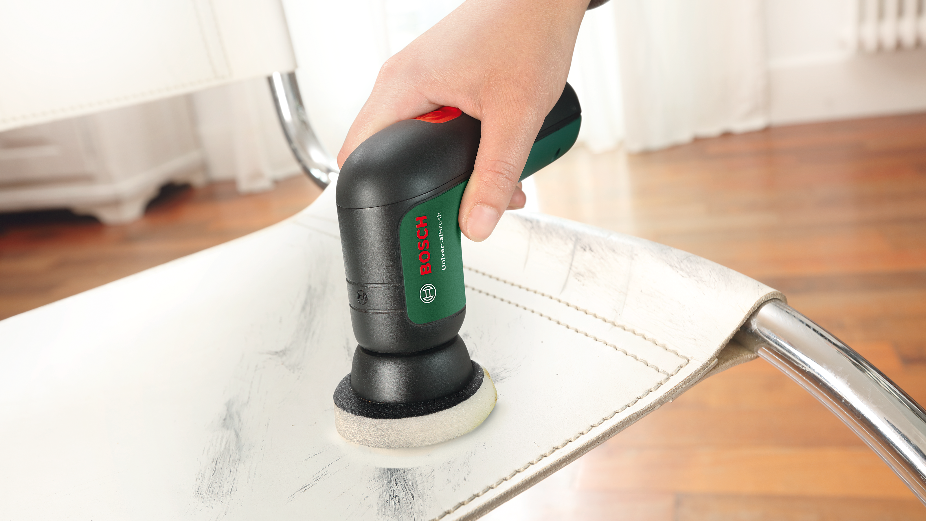 Eine Hand hält einen schwarzen Bosch Universalbürsten-Reiniger auf einem weißen Stuhl.