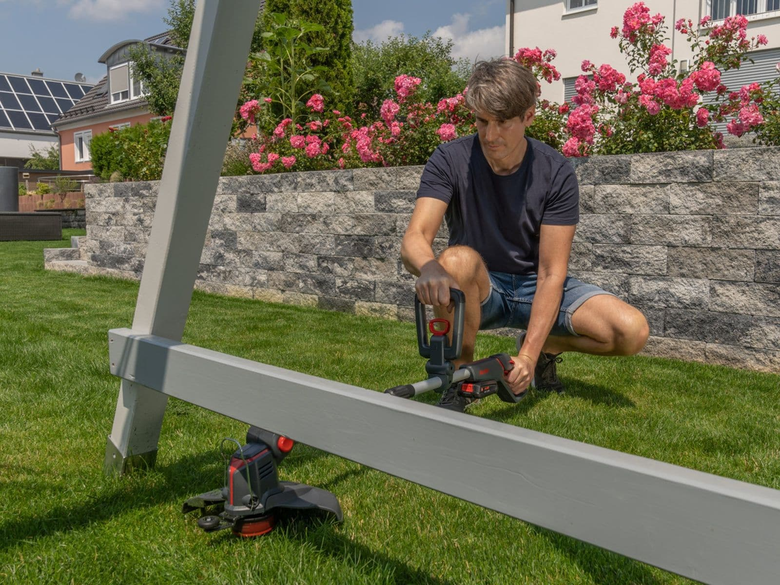 Mann repariert Holzkonstruktion im Garten mit einem Trimmer.