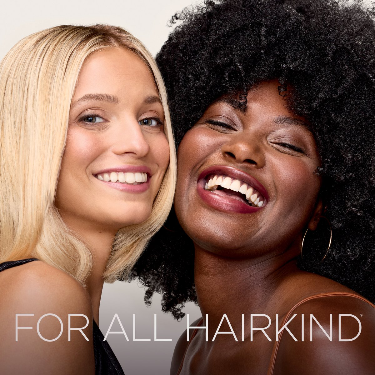 Twee lachende vrouwen, één met blond stijl haar, de ander met zwart krullend haar.