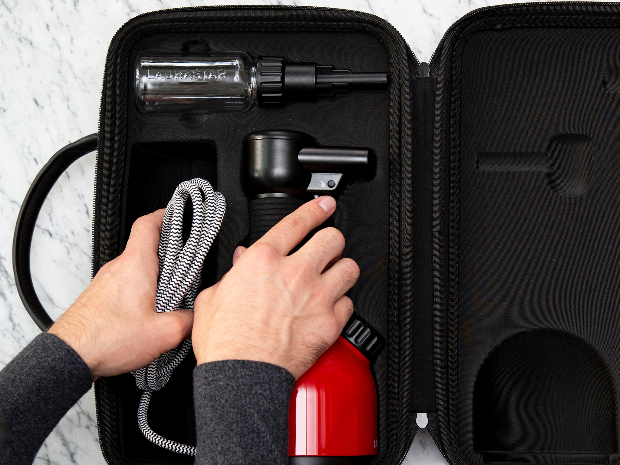 Hände packen ein schwarz-weiß gestreiftes Kabel und einen roten Behälter in einen schwarzen Koffer.