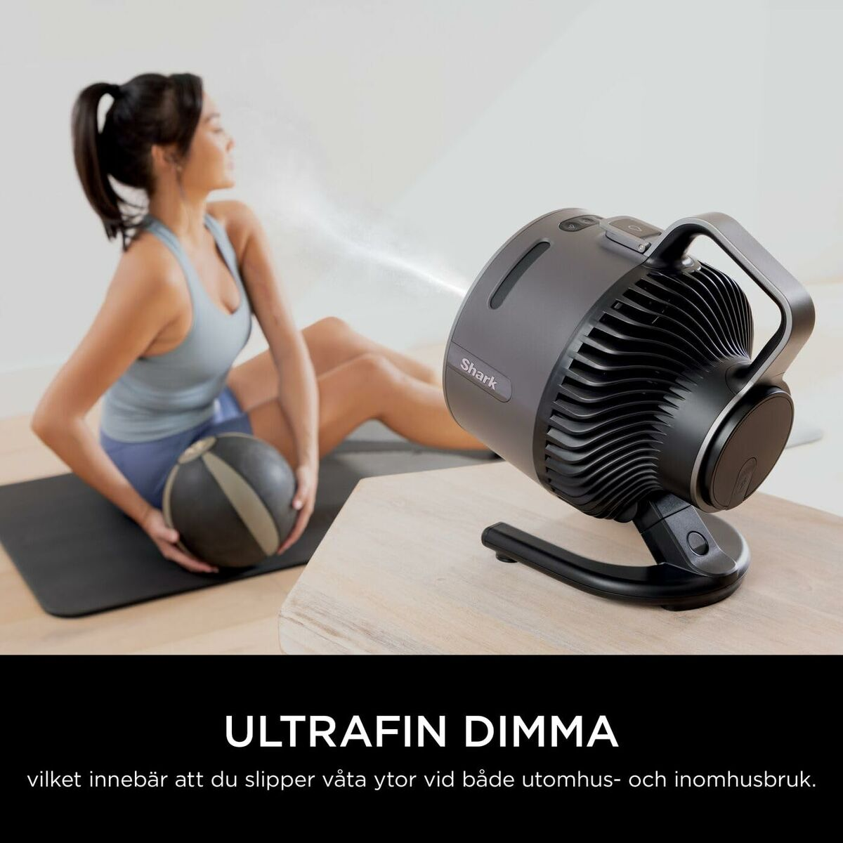 Woman on mat with ball, grey fan sprays fine mist.