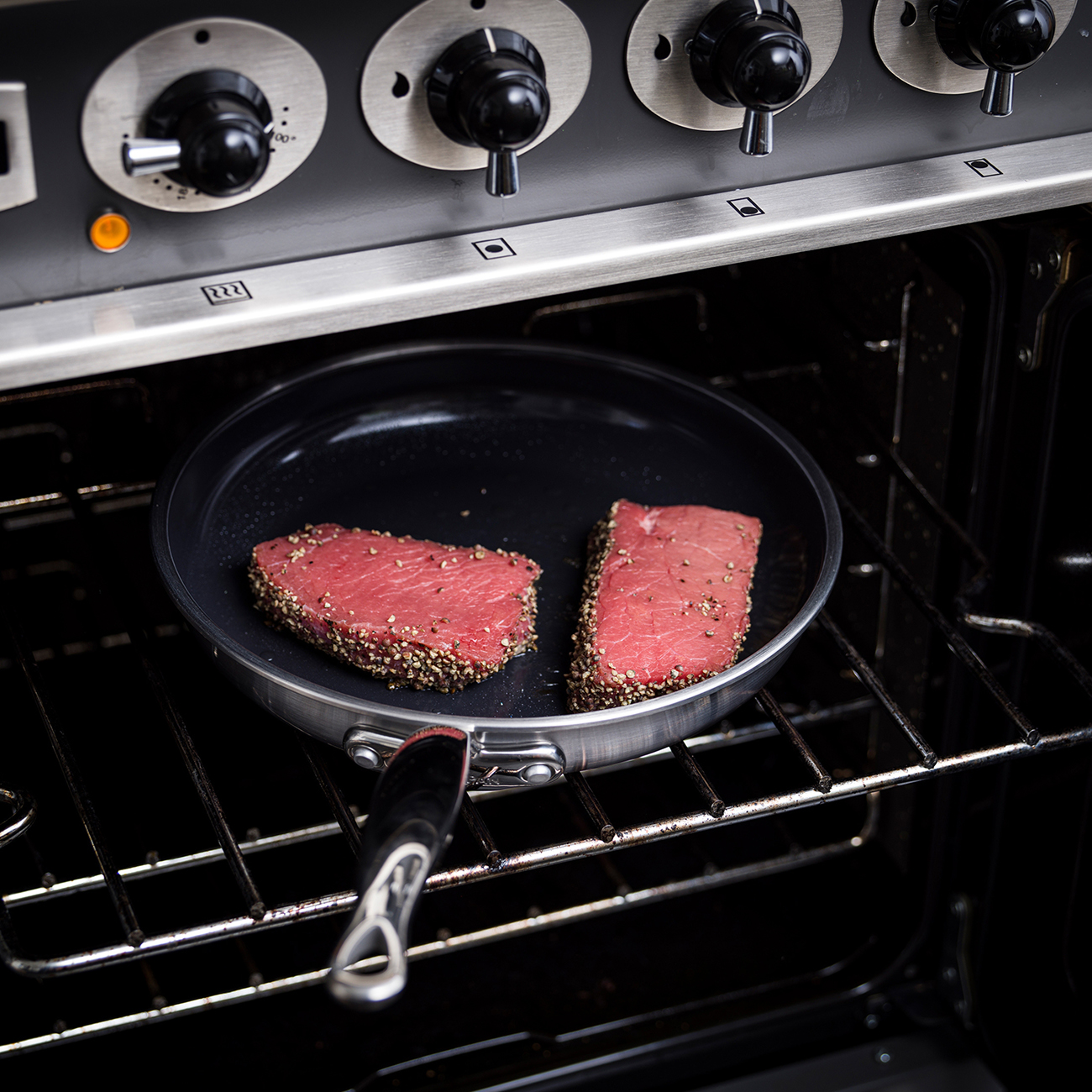 Zwei mit Pfeffer gewürzte Rindersteaks in einer Pfanne auf einem Ofenrost.