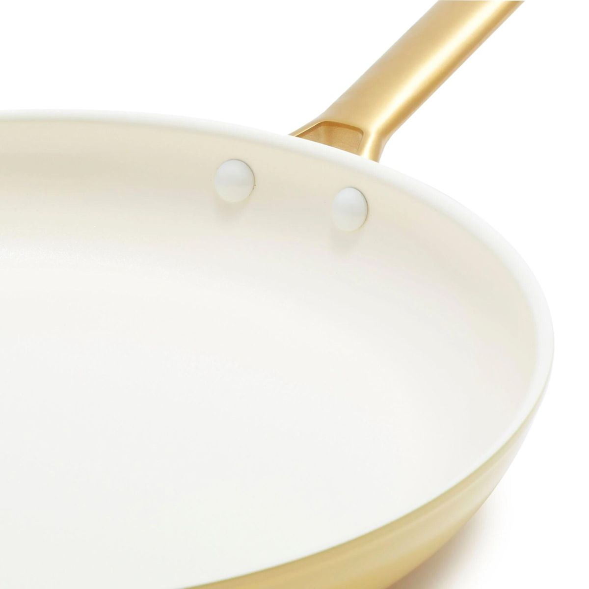 Eine cremefarbene Pfanne mit einem goldfarbenen Griff und weißen Nieten.