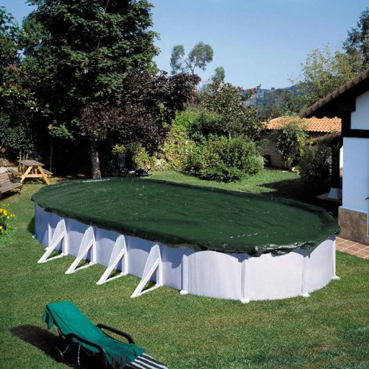 Ovaler Pool, bedeckt mit dunkelgrüner Plane, in einem grasbewachsenen Hinterhof mit Bäumen und Haus.