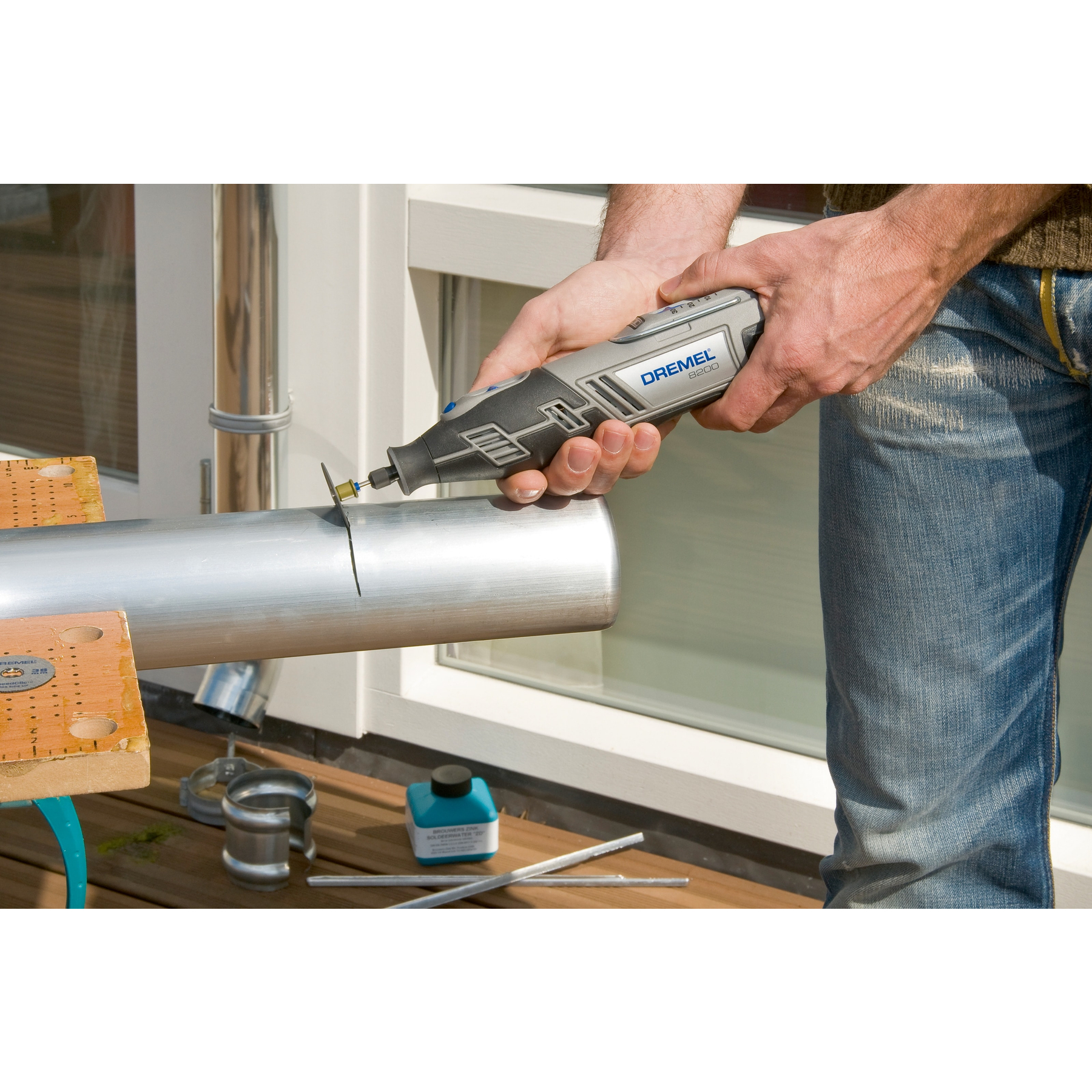 Ein Mann schneidet mit einem Dremel ein Metallrohr auf einem Holzbrett.
