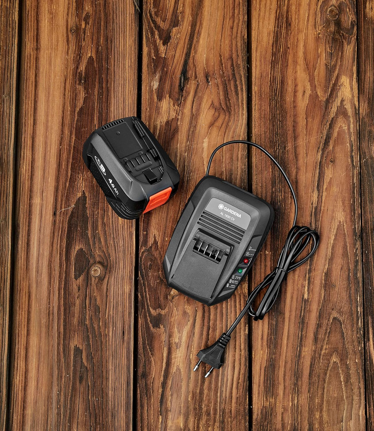 Batteria e caricabatterie Gardena su superficie in legno. Batteria nera con accenti arancioni.