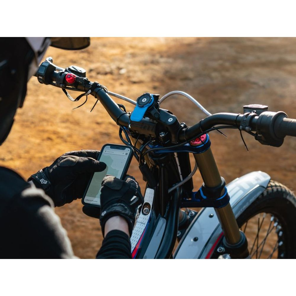 Motorradfahrer mit Handschuhen prüft ein Smartphone auf dem Lenker.