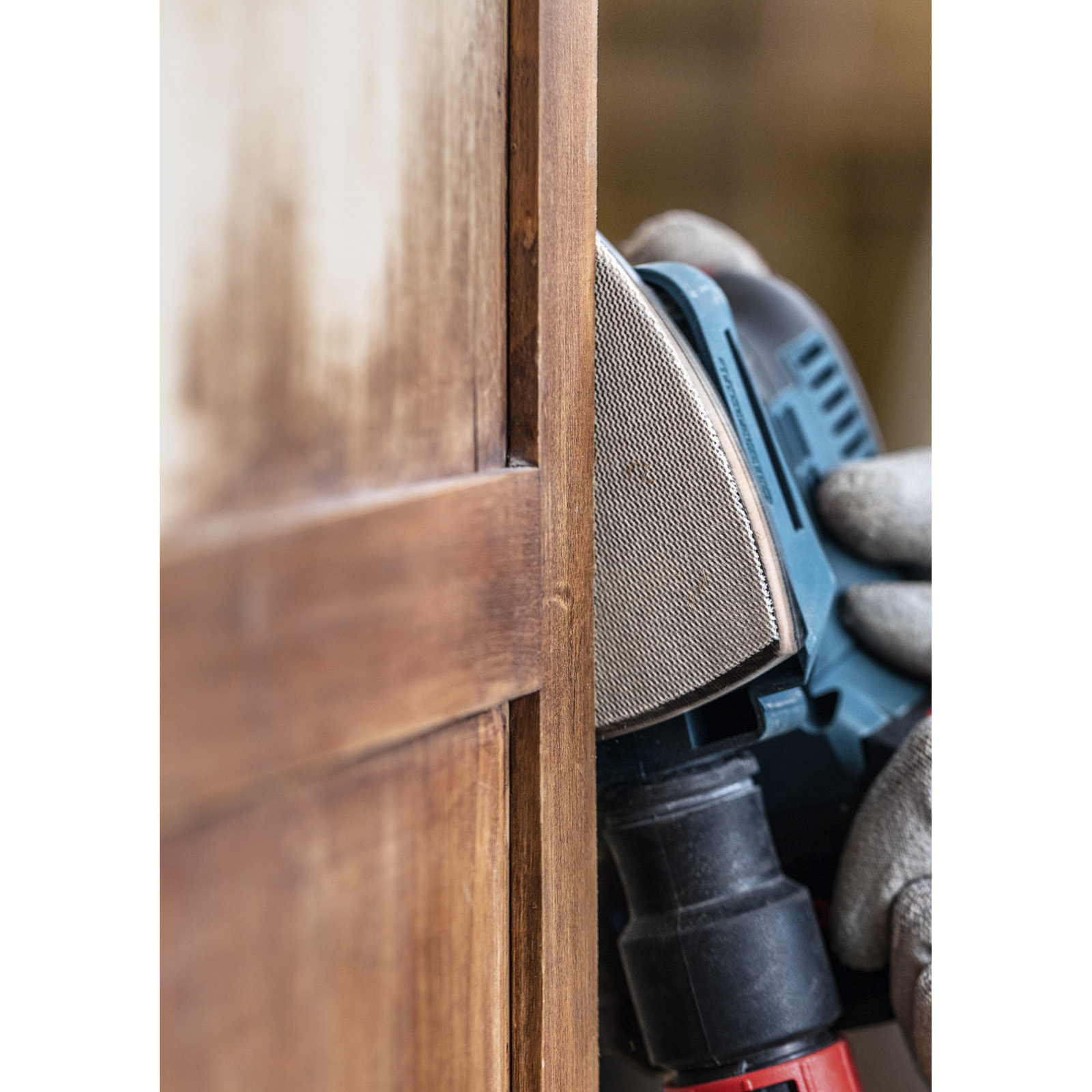 Person schleift Holzmöbel mit blauem Schleifgerät und Handschuhen.