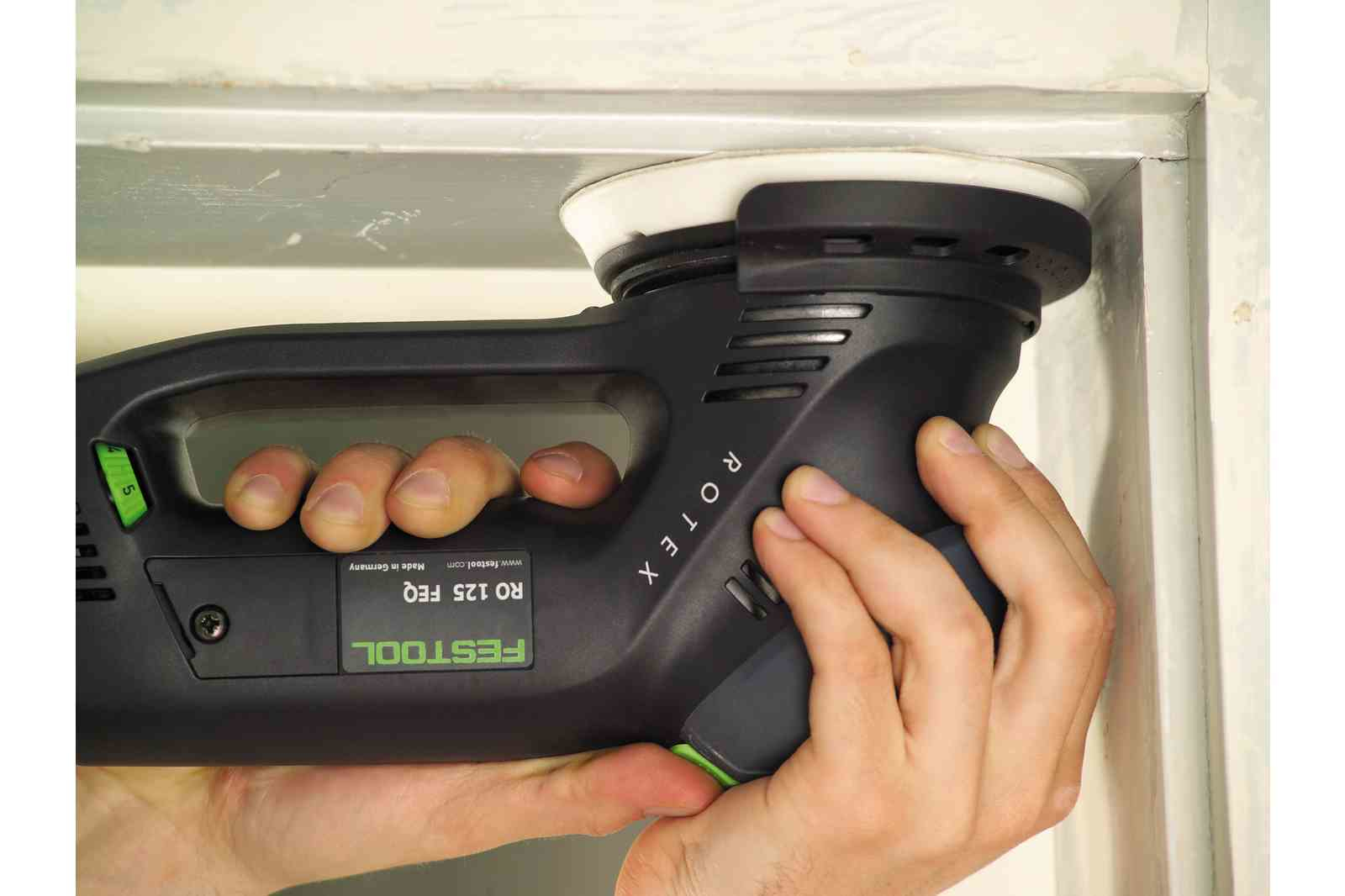 Eine Person schleift mit einem schwarzen Festool Exzenterschleifer eine weiße Ecke ab.