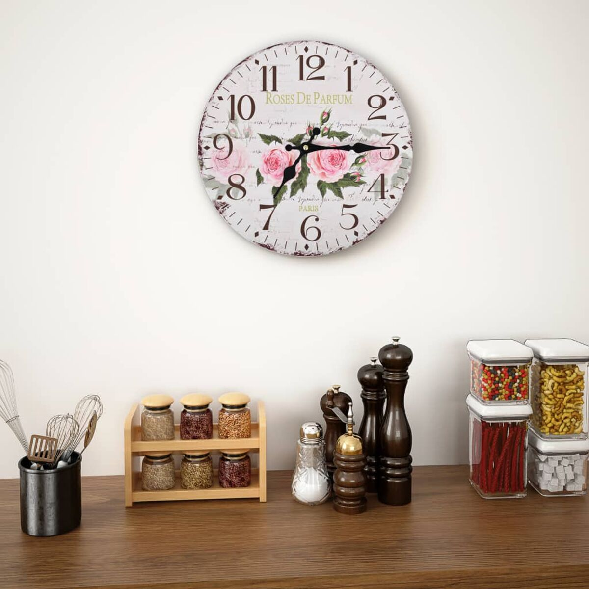 Eine runde Wanduhr mit rosa Rosen und Schrift über einer Küchenzeile mit Gewürzgläsern.