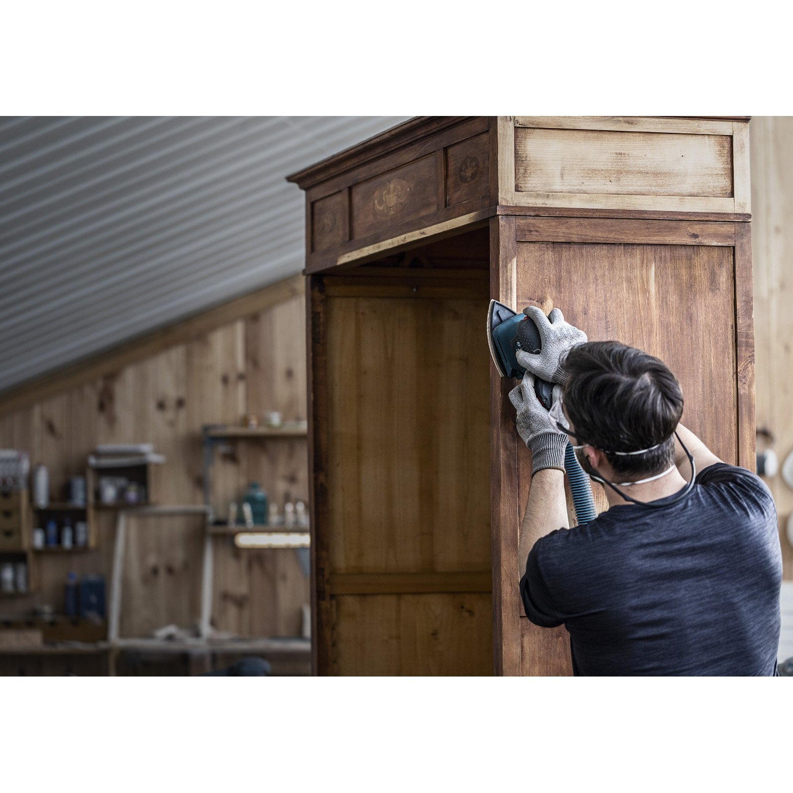 Mann schleift eine Holztür mit einem Exzenterschleifer in einer Werkstatt.