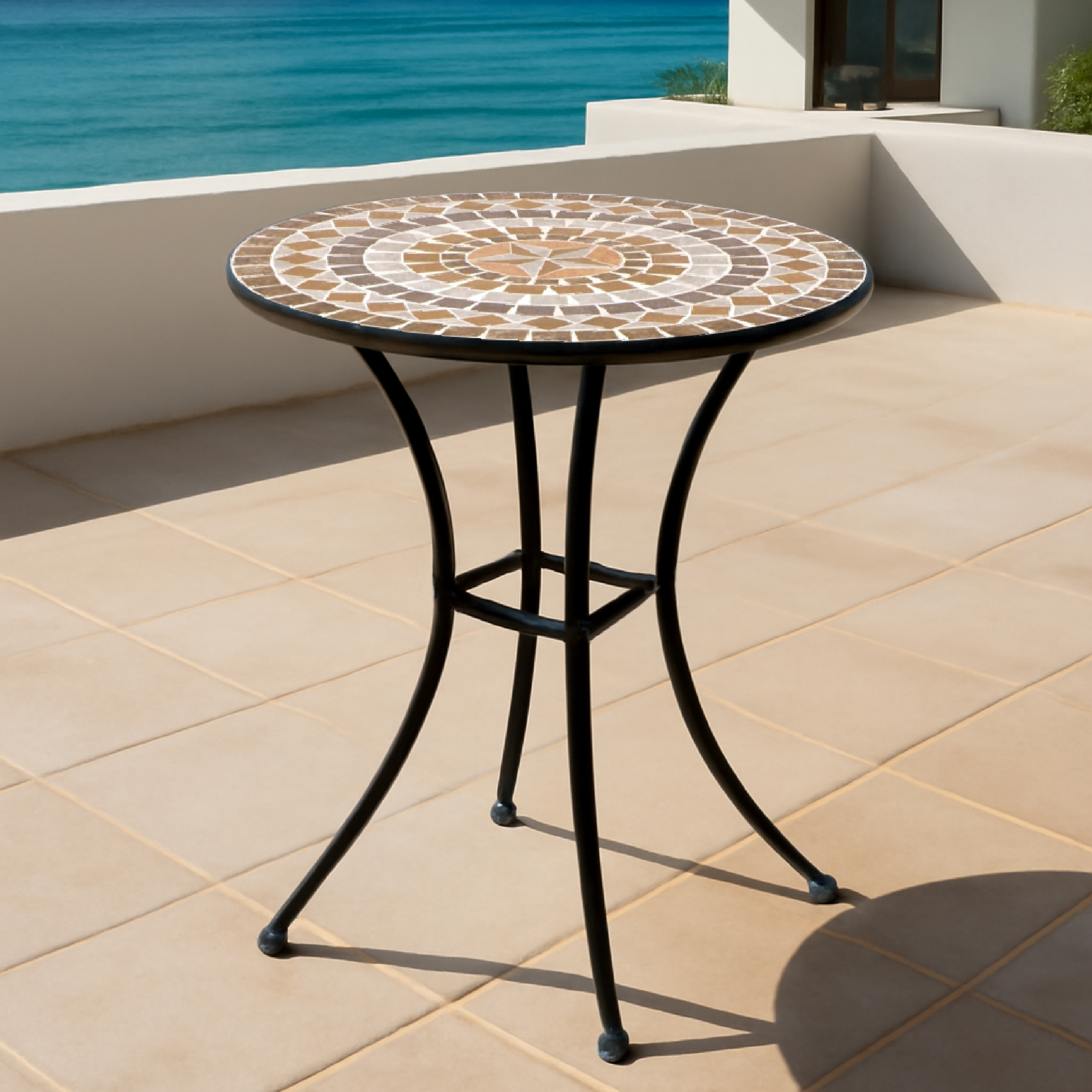 Ein runder Mosaiktisch mit schwarzem Metallgestell steht auf einer gefliesten Terrasse mit Blick aufs Meer.
