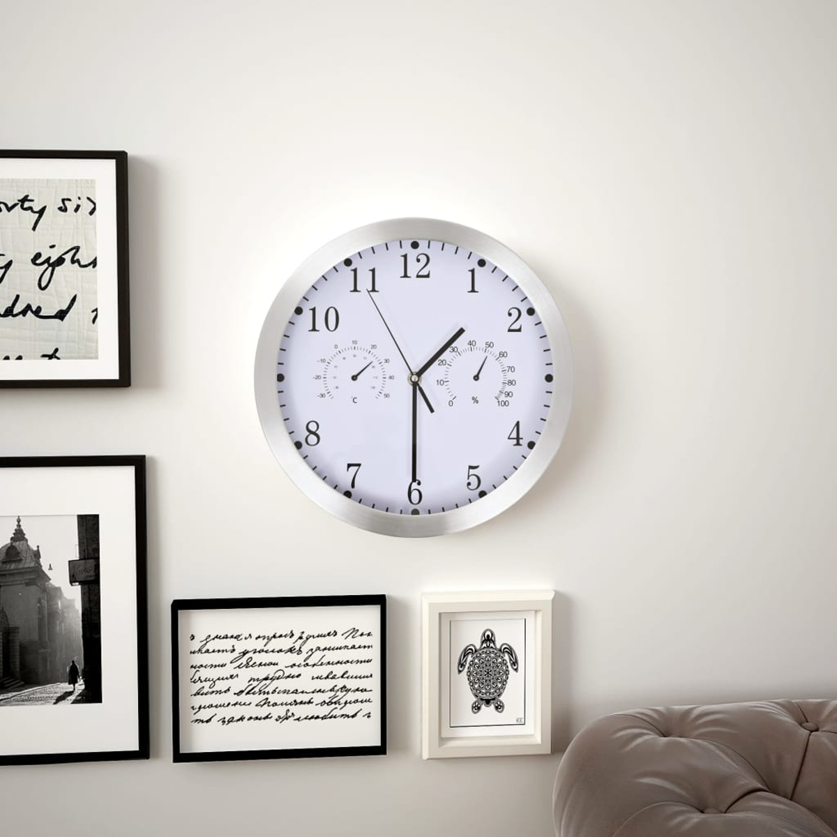 Eine Wanduhr mit Thermometer und Hygrometer hängt neben Bildern.