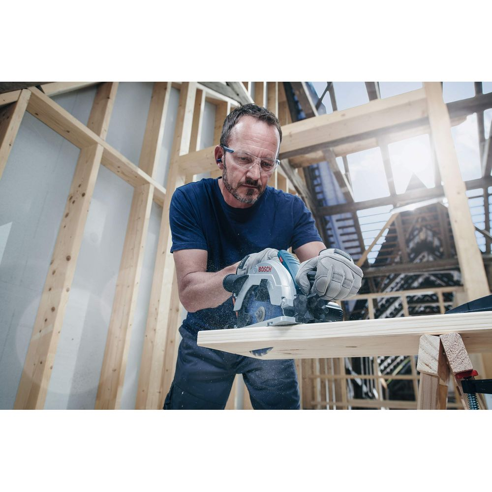Mann mit Schutzbrille schneidet Holz mit Kreissäge in einer Baustelle.
