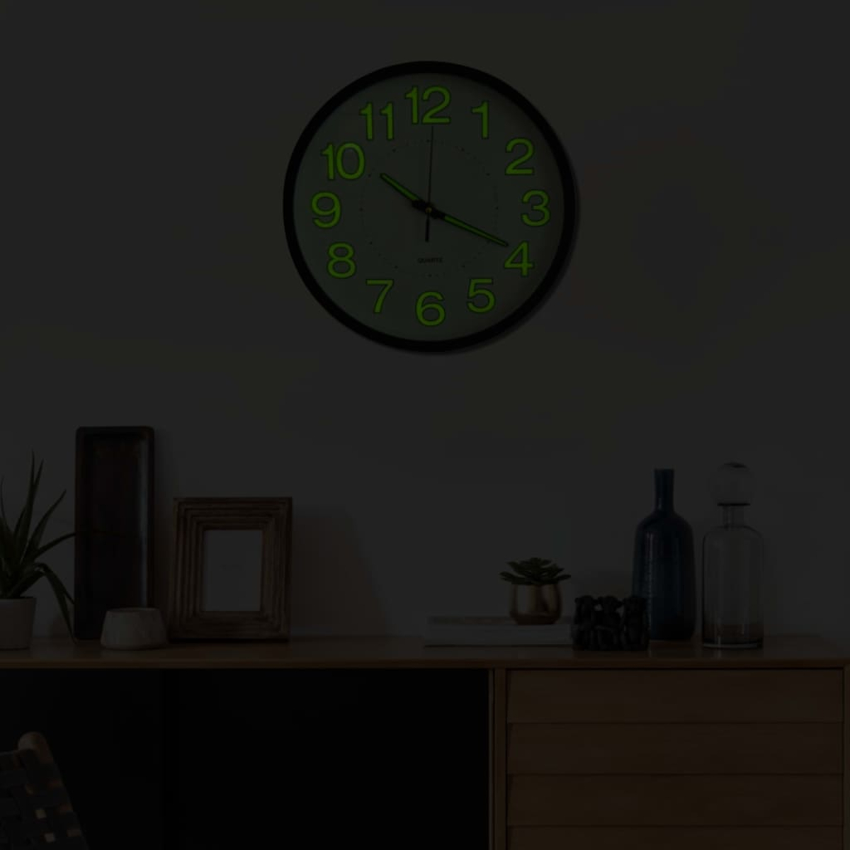 Eine leuchtende Wanduhr über einem Sideboard mit Dekorationsgegenständen.