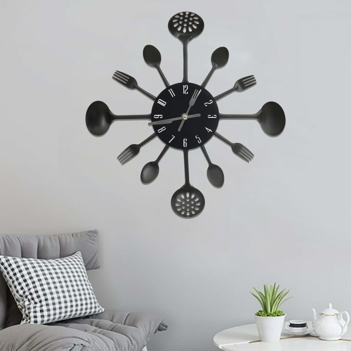 Eine schwarze Wanduhr mit Besteck-Design, die an einer weißen Wand hängt.