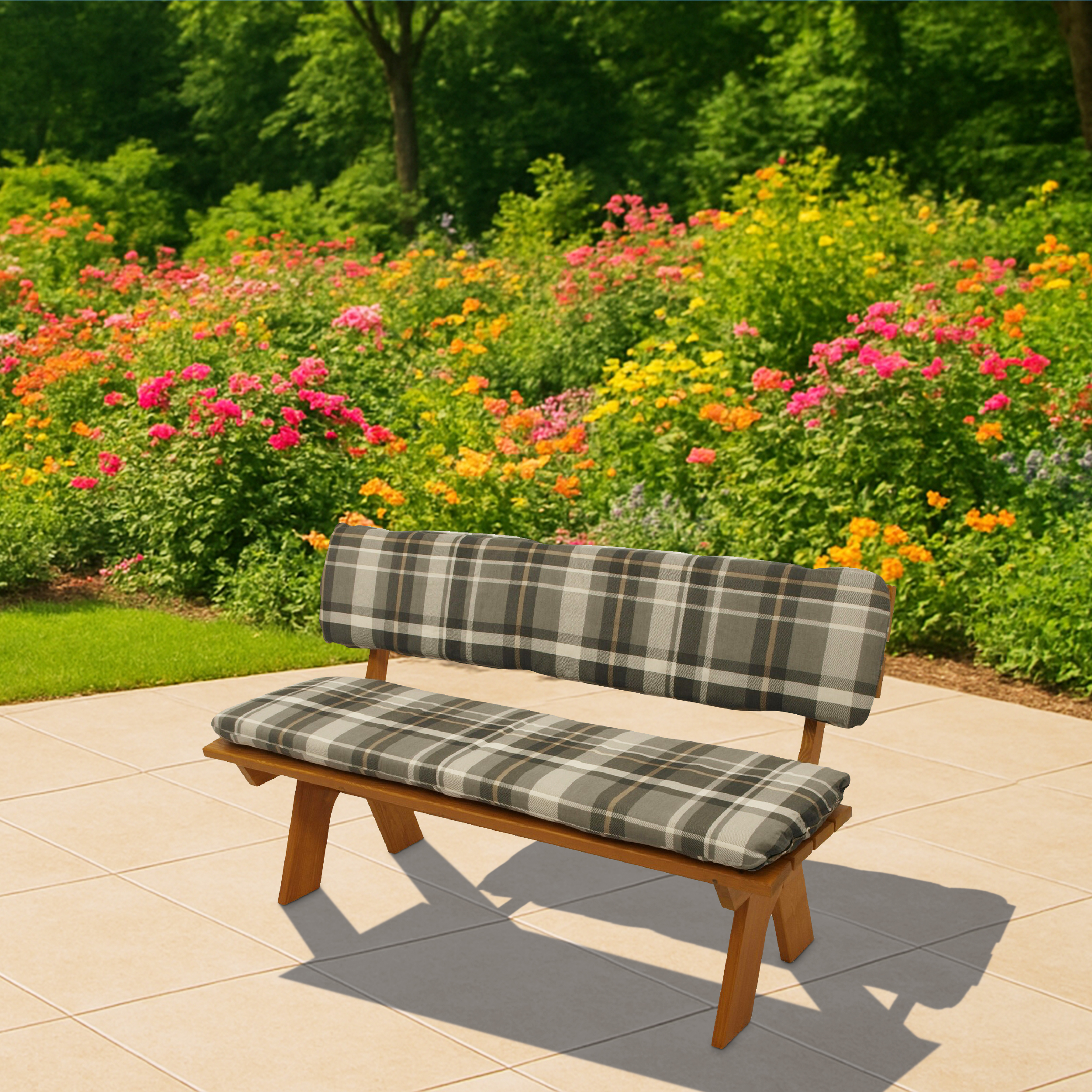 Eine Holzbank mit karierten Kissen steht auf einer gefliesten Terrasse, im Hintergrund blühende Blumen.