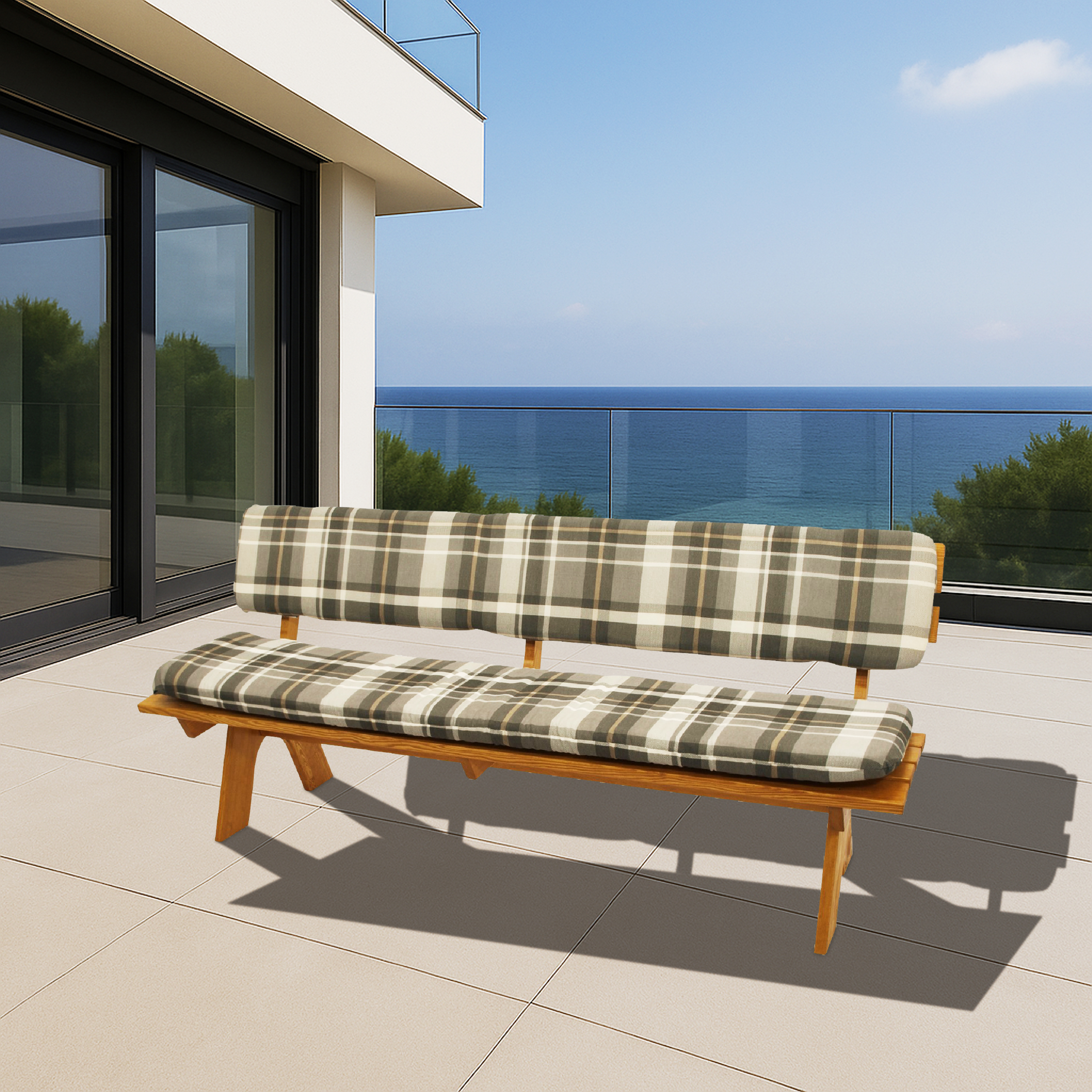 Eine Holzbank mit karierten Polstern steht auf einer Terrasse am Meer.