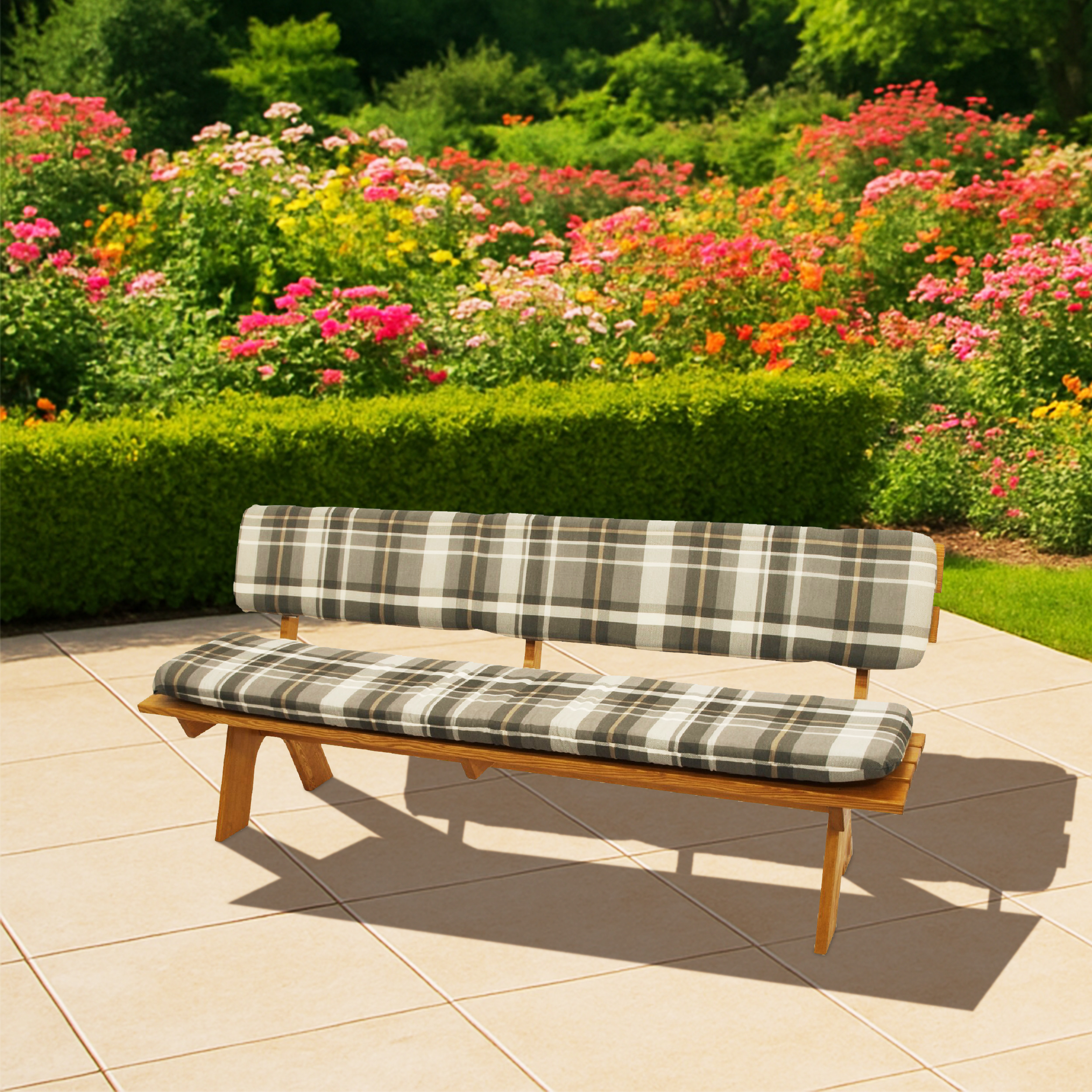 Holzbank mit karierten Kissen auf einer gefliesten Terrasse, blühende Rosenhecke im Hintergrund.