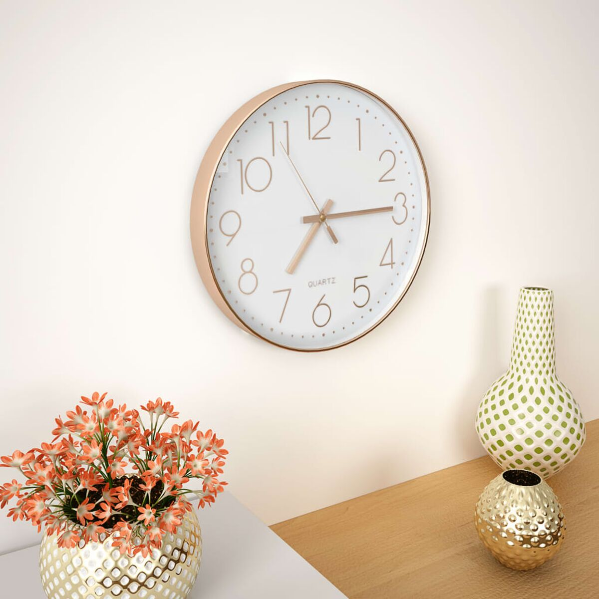 Weiße Wanduhr mit roségoldfarbenem Rahmen, daneben eine Vase mit Blumen und zwei weitere Vasen.