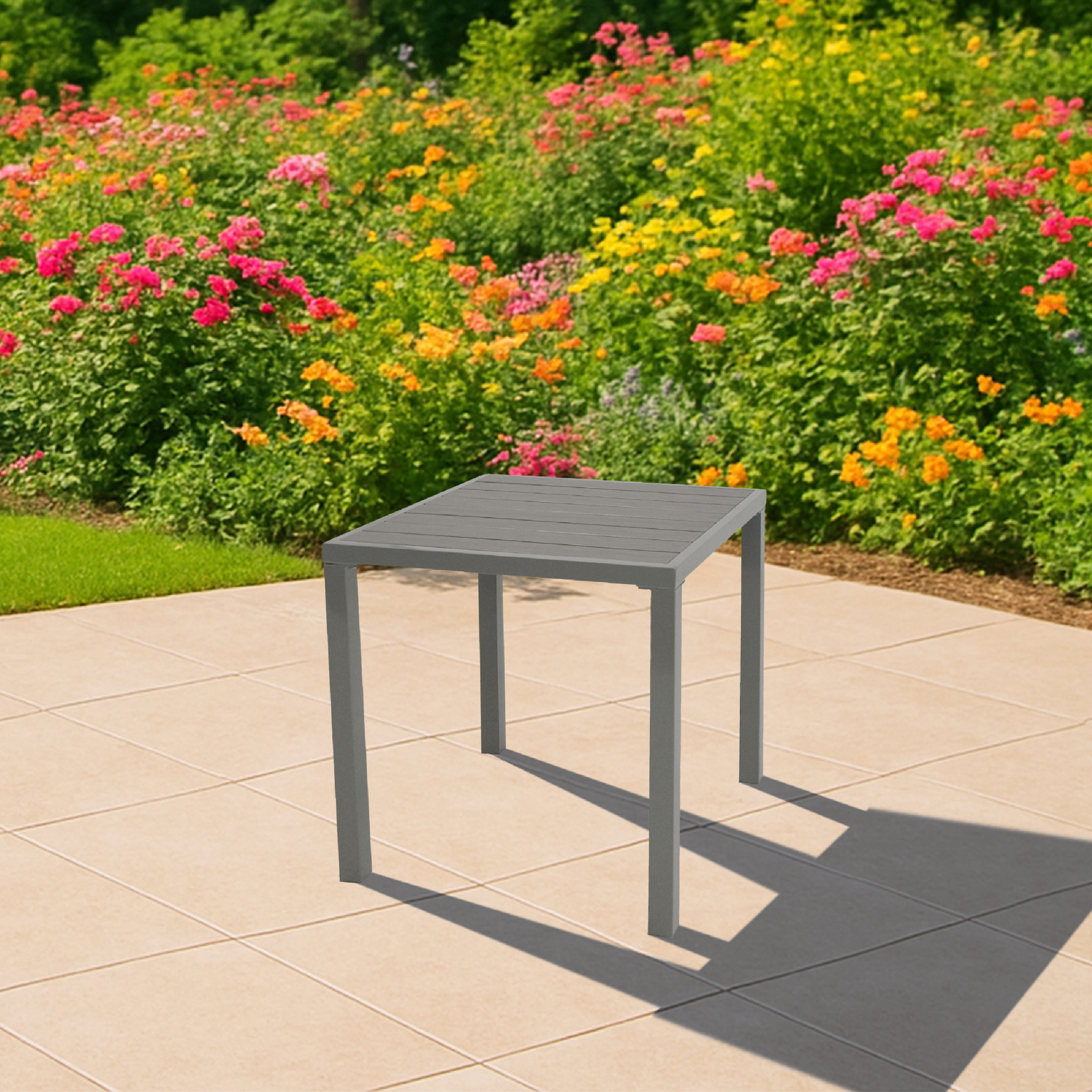 Grauer Tisch auf einer gepflasterten Terrasse mit blühenden Blumen im Hintergrund.