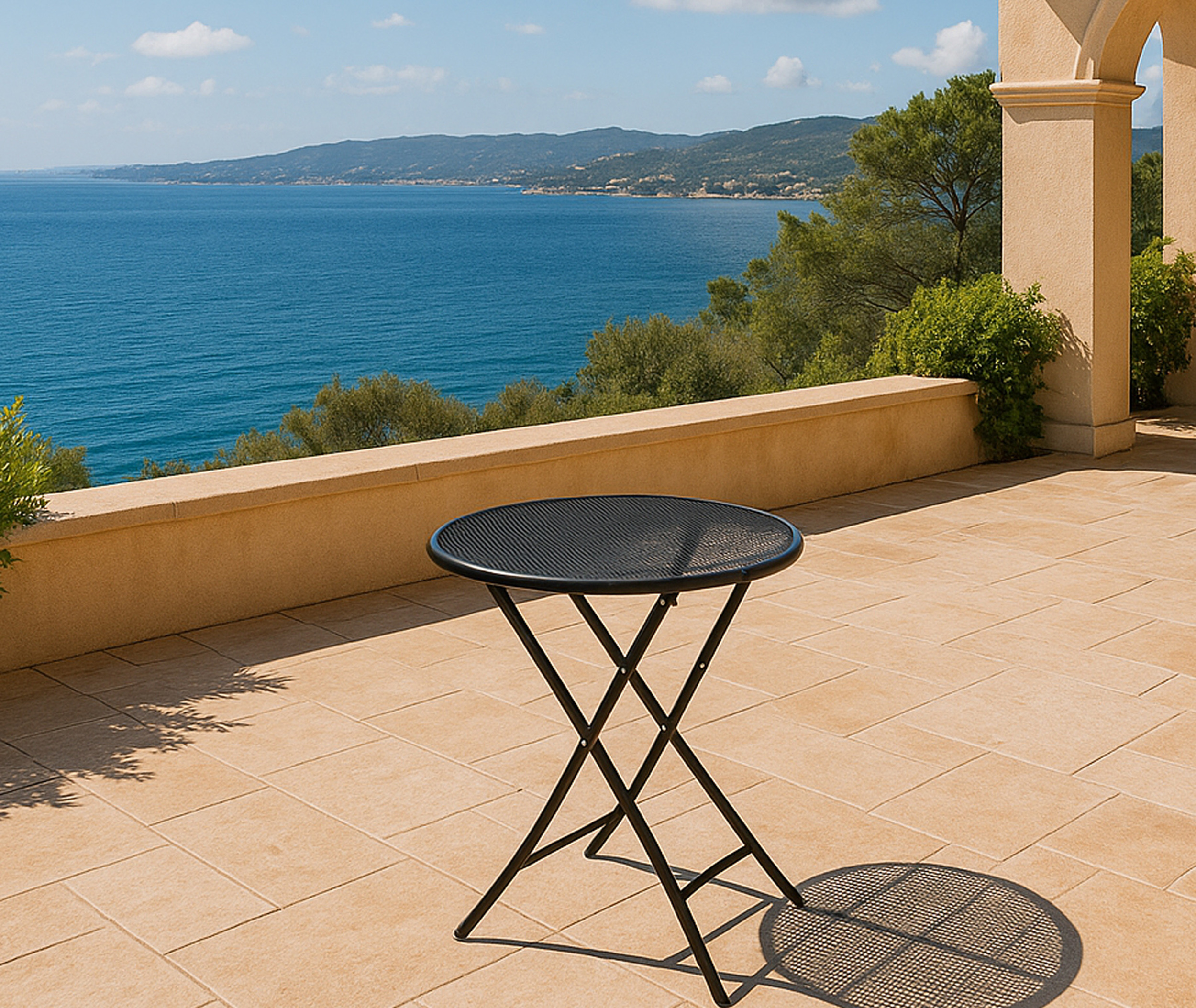 Ein runder schwarzer Metalltisch steht auf einer gefliesten Terrasse mit Meerblick.