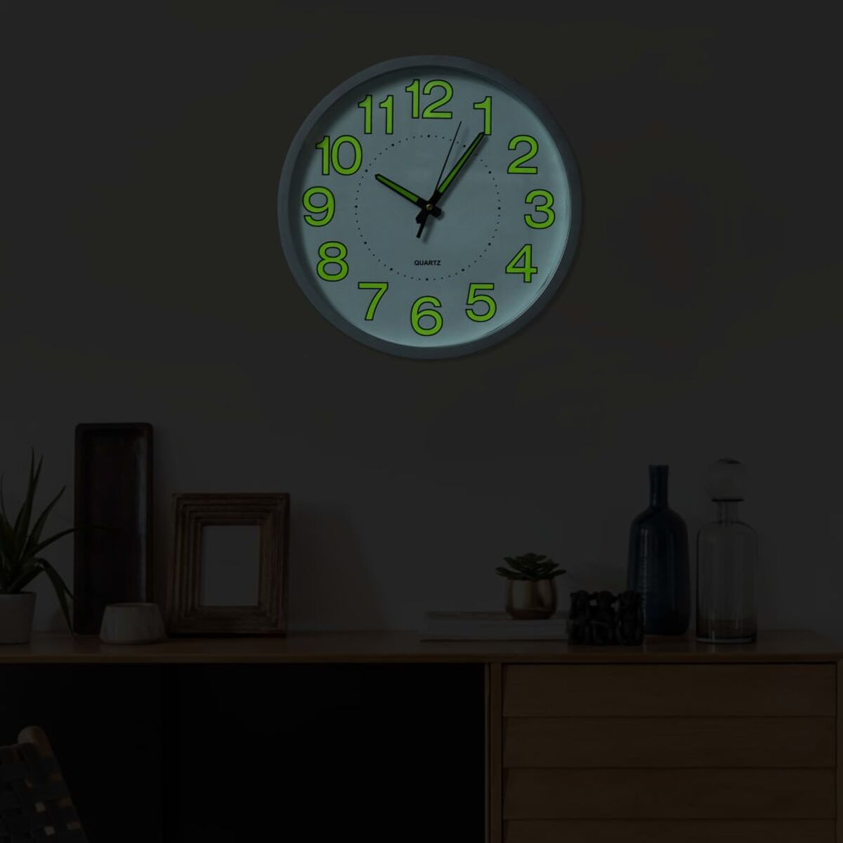 Eine graue Wanduhr mit leuchtend grünen Zahlen hängt an einer dunklen Wand.