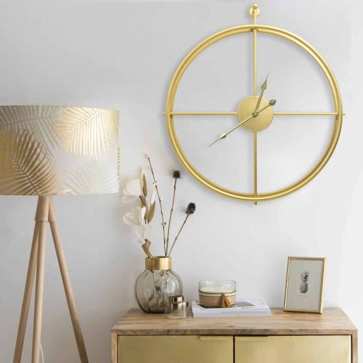Goldene Wanduhr über einem Holztisch mit Lampe, Vase und Kerze.