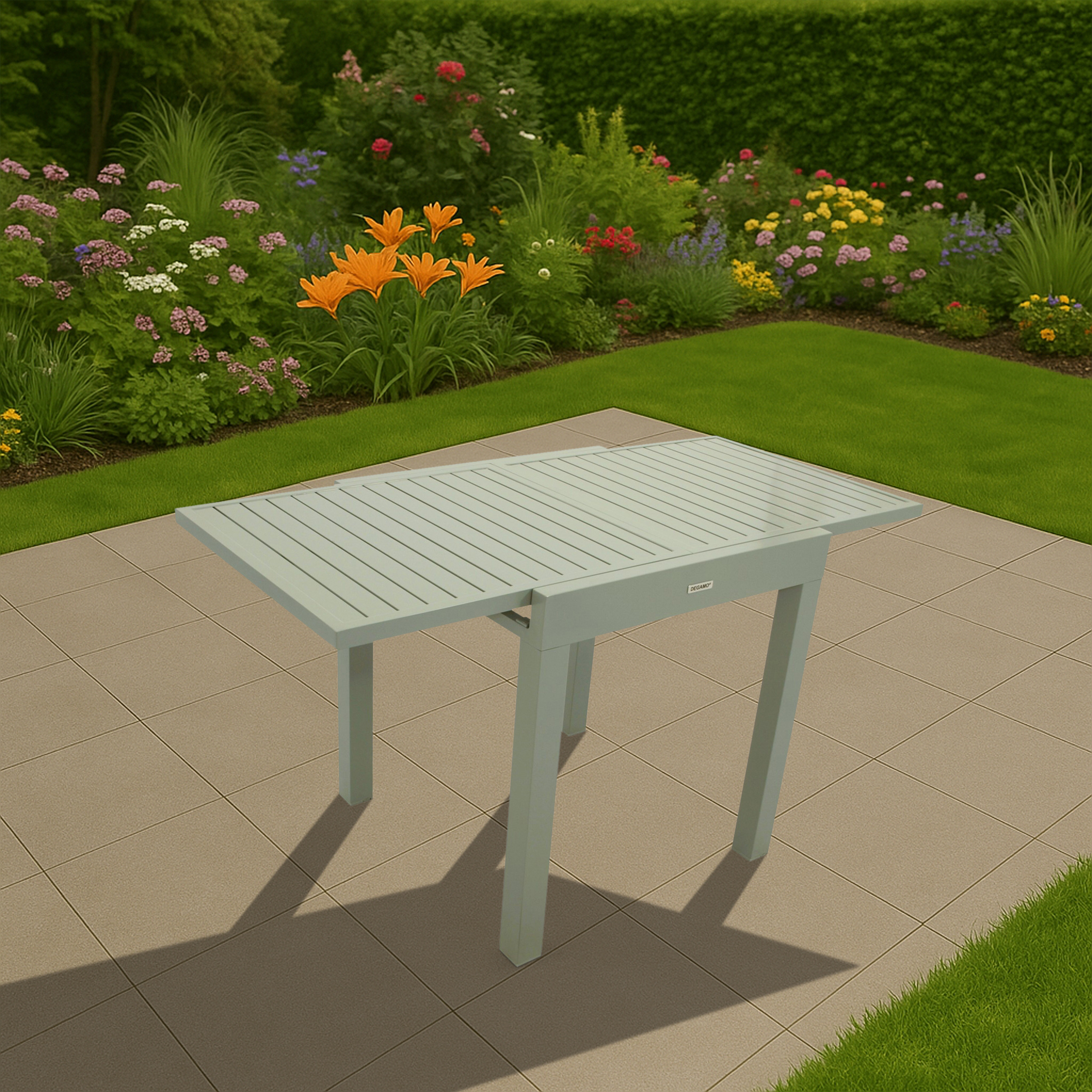 Ein hellgrüner Tisch steht auf einer Terrassenfliese neben einem üppigen Garten mit Blumen.