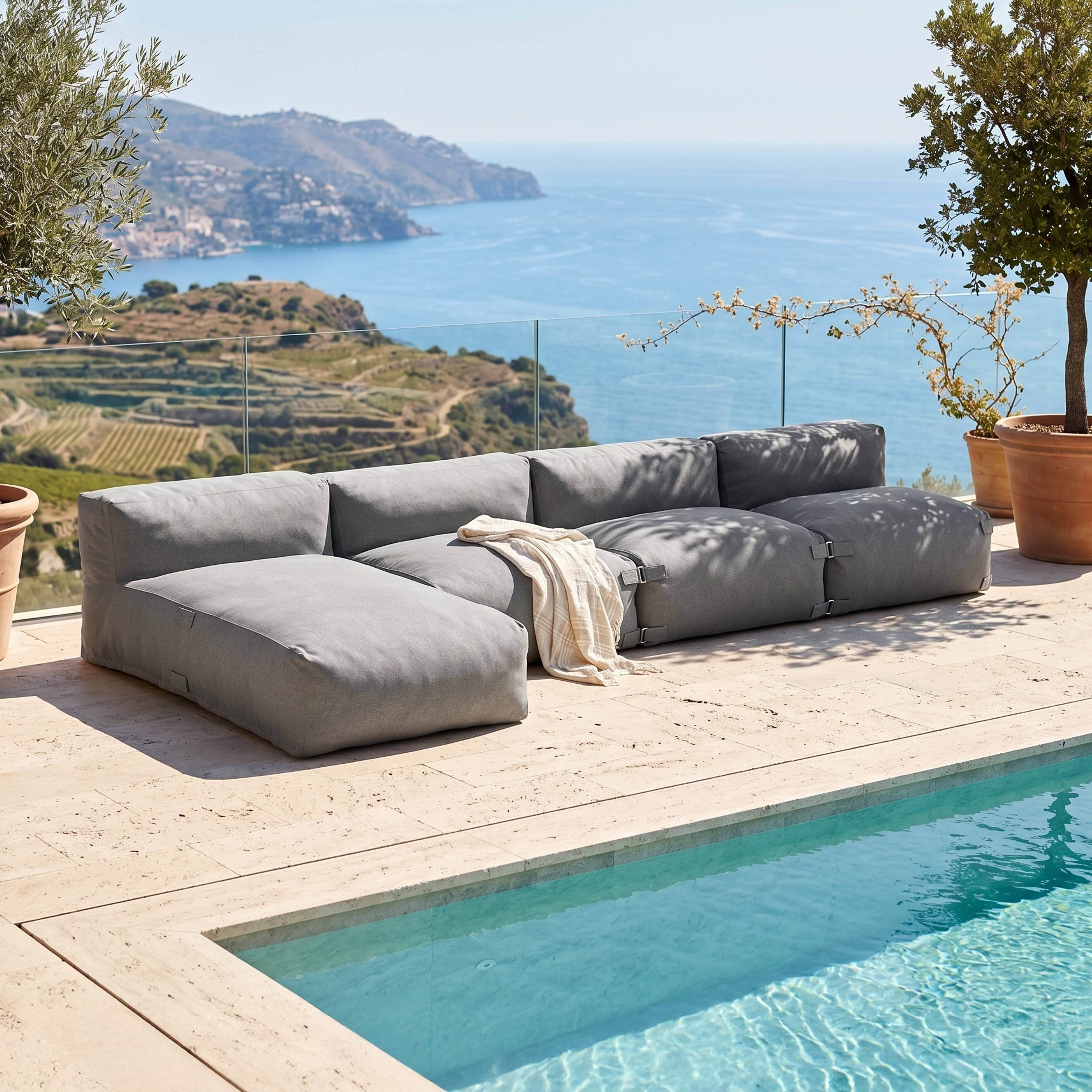 Graues Ecksofa am Pool mit Meerblick, Landschaft mit Terrassen und Bäumen.