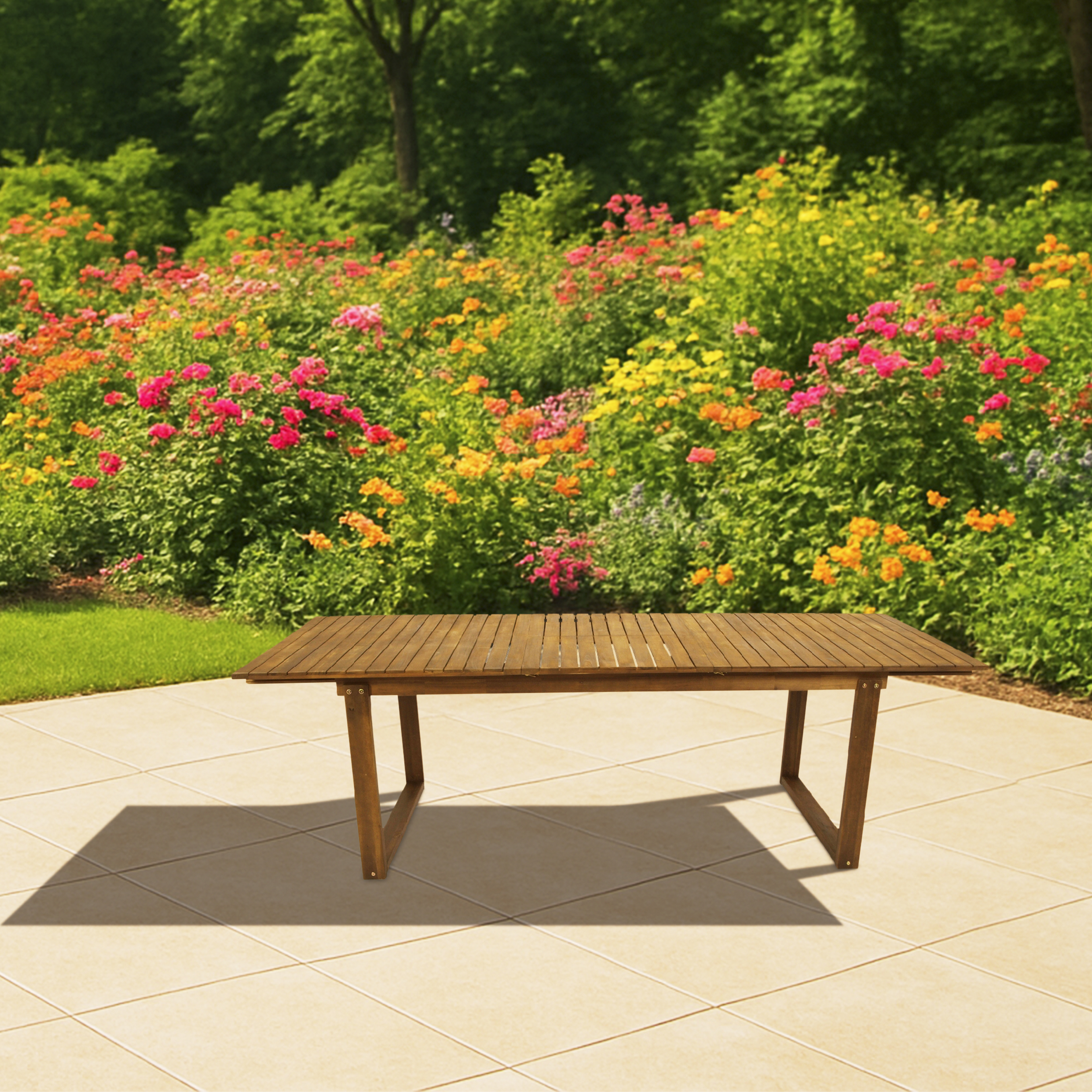 Ein Holztisch steht auf einer hellen Terrassenfliesenfläche vor einem üppigen Garten mit bunten Blumen.