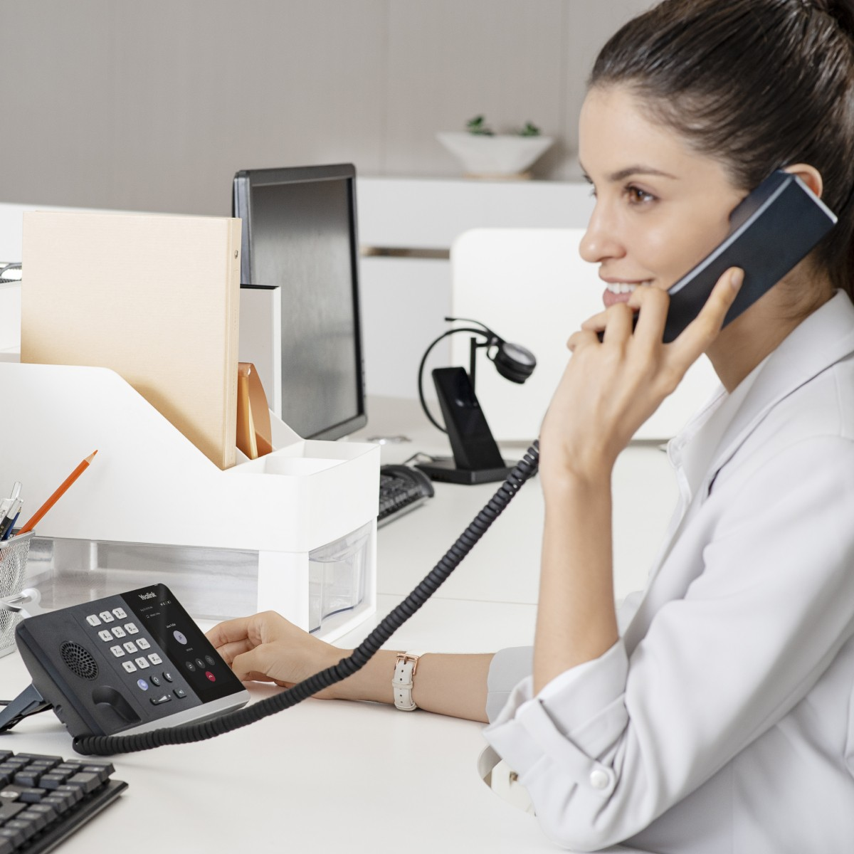 Una donna al telefono alla scrivania, con telefono e computer.