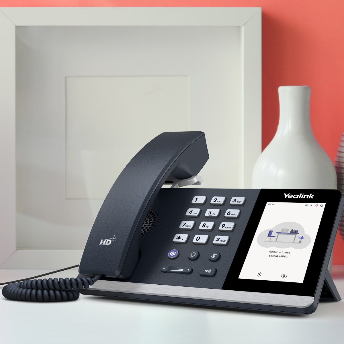 Un telefono Yealink scuro con schermo e cornetta su una scrivania bianca.